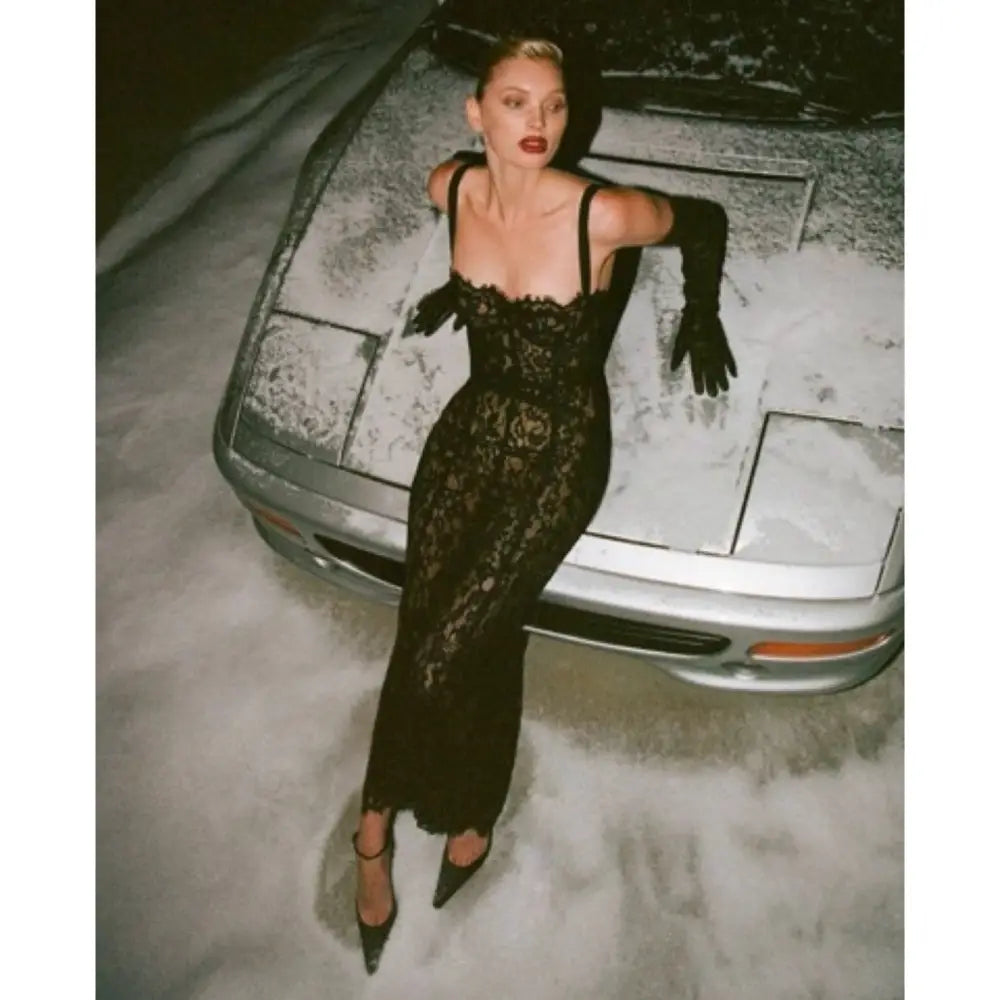 Woman in a black lace dress leaning against a car in a snowy setting